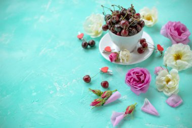 Beyaz fincan tatlı kiraz çilek gül ve çiçek bir yeşil zümrüt background.ripe kiraz ve yaban gülü. Düz yatıyordu, en iyi görünüm yiyecek çiçek arka plan. Kopya alanı