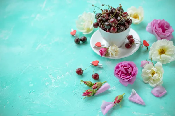 Beyaz fincan tatlı kiraz çilek gül ve çiçek bir yeşil zümrüt background.ripe kiraz ve yaban gülü. Düz yatıyordu, en iyi görünüm yiyecek çiçek arka plan. Kopya alanı