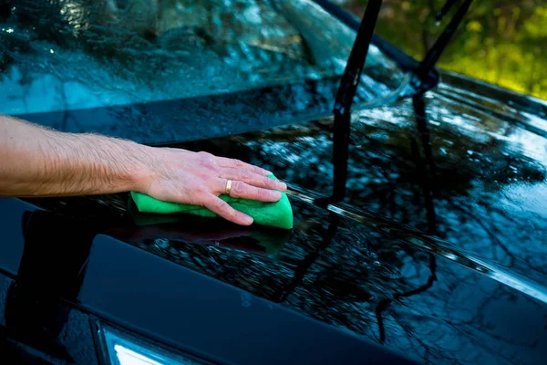 En man tvättar bilen med en svamp och häller vatten på den med en slang. Nära-up.cleaning bil med svamp på biltvätt. Bil tvätt koncept. Kopiera utrymme — Stockfoto
