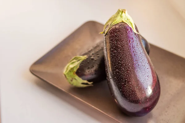 Close-up view of wet eggplants, aubergines fruit with drop water isolated on plate on white background.Raw aubergine with water drop.Wet fresh eggplant