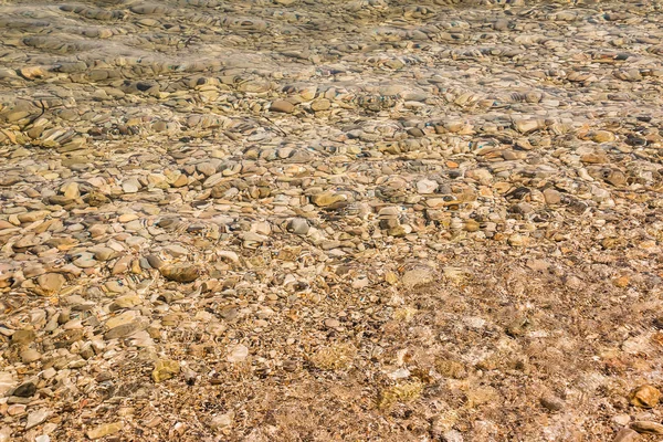 Playa de guijarros con textura de agua de mar azul fondo.Patrón de piedra bajo el agua en un hermoso día soleado de verano . — Foto de Stock