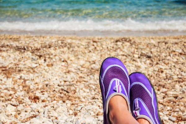Female legs with Swimming neoprene shoes.Water shoes, swimming shoe in purple neoprene on rocks in water on beach. Coral slippers on rocky beach — Stock Photo, Image