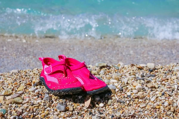 Coral slippers. Summer girl shoes for stones beach.Pink water shoes. Shoes which protect foot on a beach.Summer vacation background with a pair of sandals on beach.Copy space — Stock Photo, Image