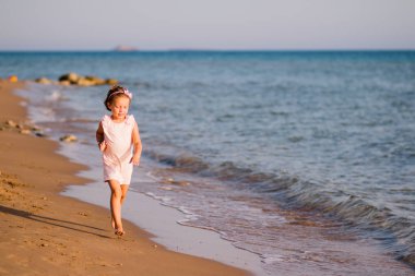 Gün batımında sahilde çalışan pembe elbiseli küçük kız. Çekimde göster. Mutluluk, tatil, fun.happy şirin çocuk ishal üstünde kumlu beach.sunny yaz günü. Kopya alanı