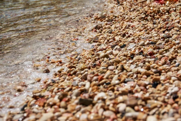 De golven van de zee met vele mooie beach pebbles textuur achtergrond. Strand met wit, gele en grijze stenen zacht afgerond. Kiezelstrand en de zee met de golven — Stockfoto