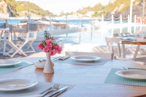 Yaz teras restoran. Şarap, gözlük ve beyaz vazo pembe tropikal flowers.flowers bir tatil beldesi, boş açık restaurant masa ile beyaz plakalı döşeme tablolar