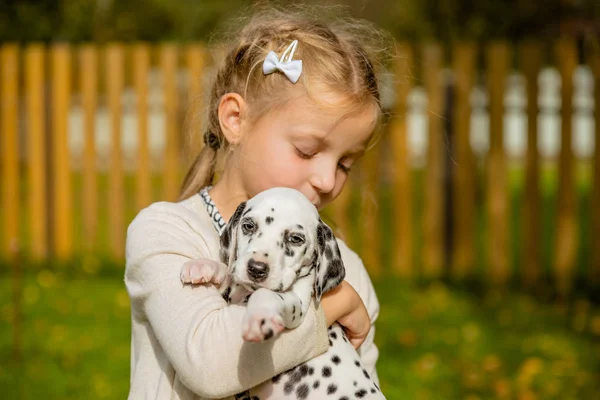 Schattige blonde meisje speelt met haar outdoo Dalmatische pup, op zonnige warme herfst day.care van huisdieren concept. Kind kussen, knuffelen van haar hond, het concept van kinderen en hond emoties, van vriendschap — Stockfoto