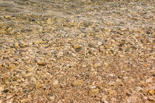 Amarillo bajo el agua peeble textura fondo. Pequeñas piedras bajo la superficie del agua. Varios coloridos guijarros húmedos textura como fondo natural . — Foto de Stock