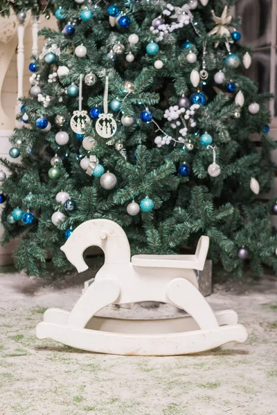 Детская игрушка качающаяся лошадь возле рождественской елки. подарки и праздники концепции. Лошадиное кресло-качалка для детей.Деревянные игрушки. — стоковое фото