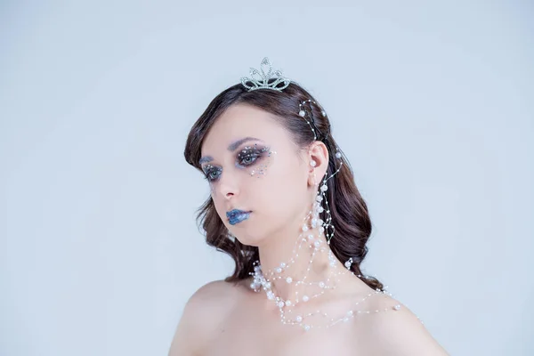 Mujer joven en imagen creativa con maquillaje artístico de plata. Maquillaje de vacaciones. Hermosa cara de mujer. Los labios de Navidad de invierno se componen y el estilo de pelo con corona. Retrato de alta moda con cristales y gemas . —  Fotos de Stock