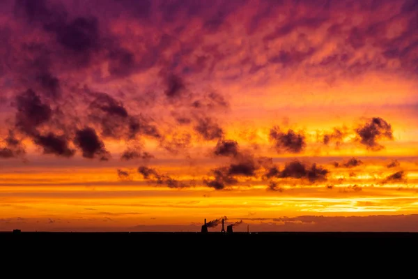 Cloudy sunset and shade of building.Dramatic red yellow sunset over the city industry. Red clouds.Panoramic view of sunset in the city with silhouette of buildings and industrial cranes, high way — Stock Photo, Image