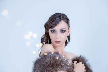 yakın çekim portre olan mükemmel sanat makyaj güzel kıvırcık kadın trendy buzlu yüz, gözleri çizmek parlak taşlarla boncuklar, yapmak kadar dekor. Noel çelenk ışıkları. Eko kürk coat.expressive gözleri. Kopya