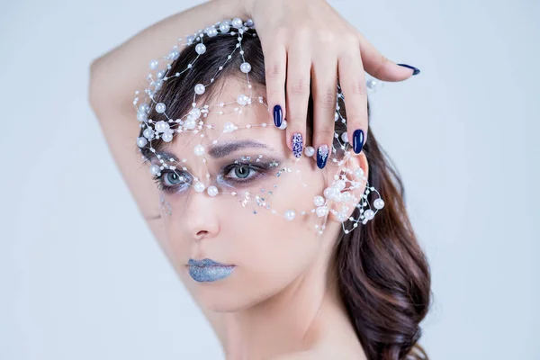 Beautiful model girl with blue manicure nail design,face and hair with beads, rhinestones ,decoration. Fashion makeup and care for hands and nails and cosmetics.Nail art design.emale beauty. Luxury