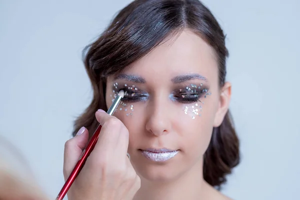 Hand puts a shadow color on the eyes a beautiful young girl.Make-up artist applying bright color eyeshadow.Creative art work.Silver lips.portrait of attractive caucasian woman, glitter face skin care