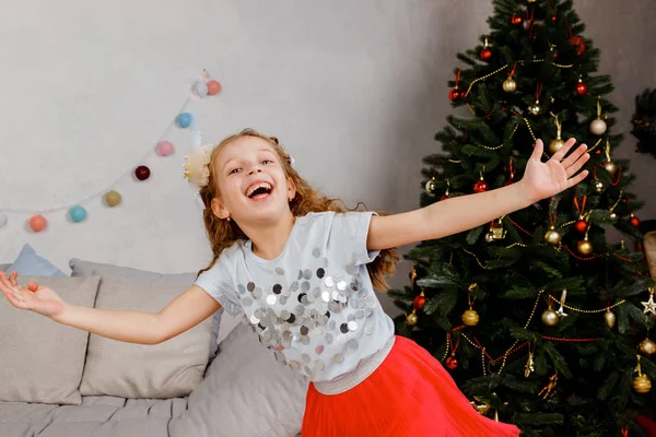 Linda niña baila en la noche de Navidad. Niño disfruta de vacaciones de invierno.Bailar, cantar, divertirse en el fondo del árbol de Navidad con guirnaldas y decoración de Navidad . —  Fotos de Stock