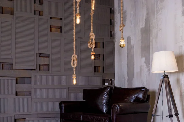 retro edison bulbs hanging, suspended to a wooden ceiling in loft, the concept of creativity.Stylish cozy scandinavian bedroom interior, leather sofa,wooden wall.loft apartment interior.Minimalist