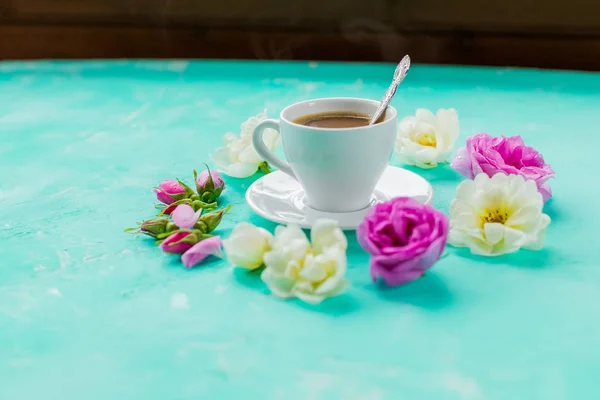 Coloridas flores y taza de café de la mañana sobre fondo azul. el concepto de bebida caliente, café para el desayuno. mesa romántica con copa de bebida caliente y rosas.beautiful flores para —  Fotos de Stock