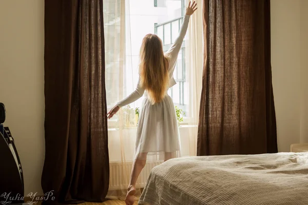 Mão abre cortina na casa de madeira Janela. A luz solar brilhante brilha. Bela luz da manhã ensolarada por trás do conceito de mundo da manhã Chalet Window.good. parte de trás da mulher silhueta — Fotografia de Stock