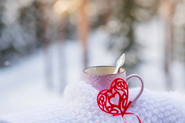 Cup with red heart and a hot drink wrapped in a scarf in the snow. Concept for Valentines day.Romantic Morning breakfast for Valentines day on snowy forest background.Hello February. vintage red — Stock Photo, Image