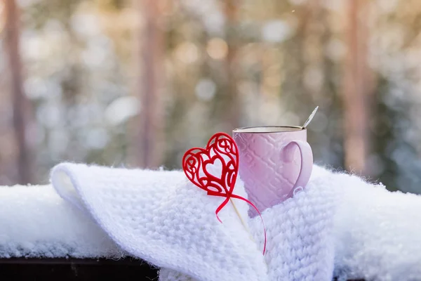 Чашка с красным сердцем и горячий напиток, завернутый в шарф на снегу. Утренний завтрак для Дня святого Валентина на заснеженной лесной задворке. винтажный красный — стоковое фото