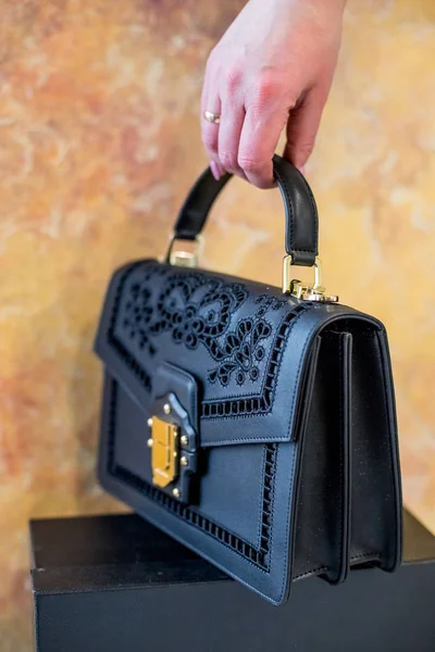 Elegant black female bag over yellow background in female hand.luxury black leather bag, fashion hand bag isolated.