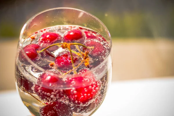 Cocktail de cereja - em água com gás - contra fundo desfocado. Bebida refrescante fria do verão com cerejas frescas. Foco seletivo. Espaço de cópia — Fotografia de Stock