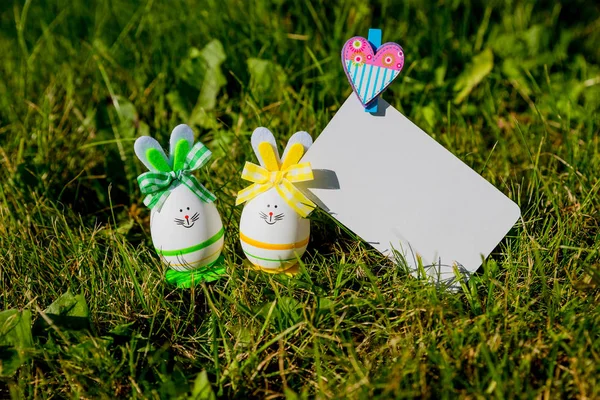 Biglietto di auguri in bianco con piccole uova di Pasqua in erba.Uova di Pasqua sul prato. Concetto vacanze primaverili. Composizione pasquale con uova di Pasqua. Biglietto d'auguri bianco Mockup — Foto Stock