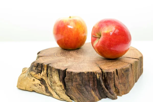 Duas maçãs suculentas vermelhas estão em um toco de madeira no fundo branco.Maçãs frescas em um tronco de madeira.Delicioso e maduro conceito de alimentação. . — Fotografia de Stock