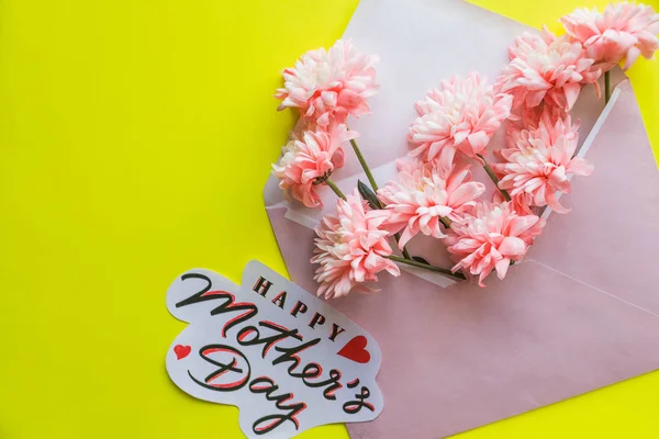 Güzel çiçek düzenlemeleri. Pembe krizantem zarfın üzerine sarı arka plan ile. Düz yatıyordu, üst view.happy anneler günü text.floral tebrik kartı kavramı