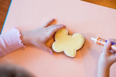 Üst görünüm, renkli el yapımı Paskalya nesneleri, fırın, tablo ve eller boyalı gösteren döşeme çerezleri, küçük, küçük kurabiye dekore. Çocuklar anne için Gingerbread çerezleri süslüyor. Mutlu anne gün prese