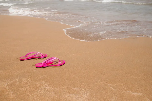 Beach pink flip-flops on a light sand. Texture of light sand. The concept of a beach holiday. Summer concept. Flat lay, side view, copy space.Tropical vacation concept — Stock Photo, Image