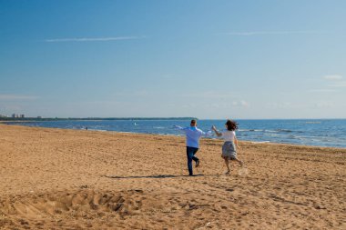 mutlu genç düğün çift adam ve beyaz rüzgar hava güneşli gün okyanus plaj kıyısı boyunca çalışan kadın. Sahilde, deniz kıyısındaki bir çift aşık. Aşk yürüyüş çift, eğlenmek