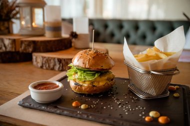 Restoranda ahşap bir tabaktabakta hamburger, patates kızartması ve bir fincan sosdan oluşan fast food akşam yemeği. Patates kızartması ile lezzetli hamburger. sandviç brunch için popüler fast food