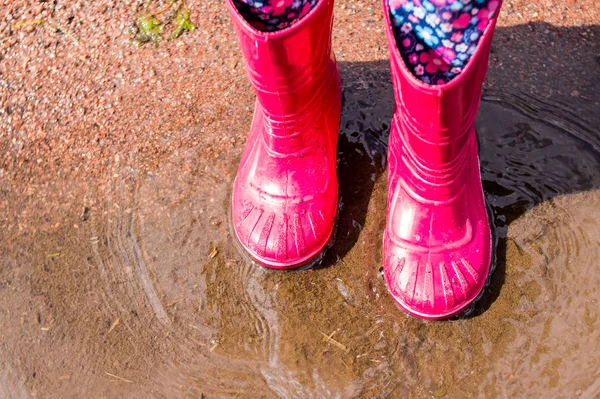 legs of child in orange rubber boots jumping in the autumn puddles. kids bright rubber boots,gardening. Rainy day fashion.Garden Rainy Rubber Shoes. boots for rainy day. Autumn kids boots concept.