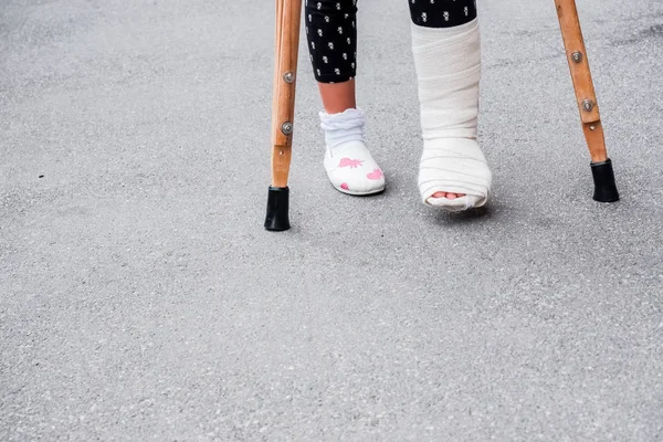 Fiatal lány ortopéd leadott mankók séta az utcán az út közelében. Gyermek egy törött lábát mankó, boka sérülés. Csonttörés és boka törés a gyermekeknél — Stock Fotó