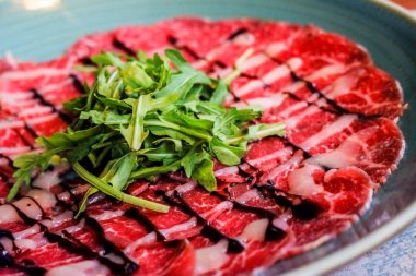 restoranda mavi plakalı arugula sığır eti carpaccio ile beyaz çanak. Sığır eti İtalyan geleneksel carpaccio, seçici odak.
