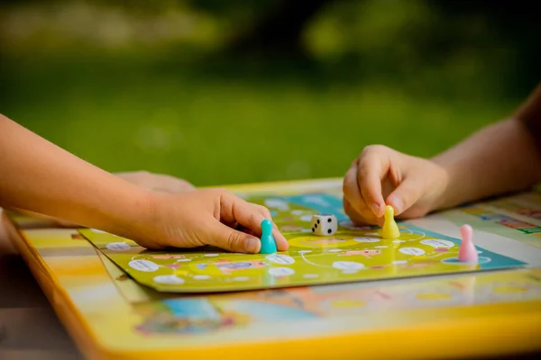 Jogo de tabuleiro e conceito de lazer para crianças. Os miúdos estão a brincar. pessoas segurando figuras na mão. chips de madeira amarelo, azul, verde e vermelho em crianças play.concept de jogos de tabuleiro. Dados, fichas e cartões. Jogo de festa — Fotografia de Stock