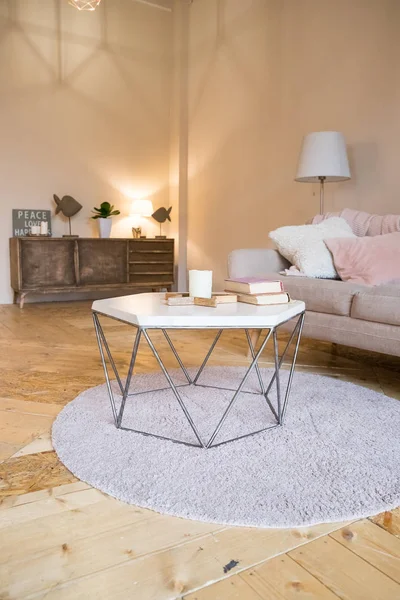 loft tarzı. Küçük tasarım masa ve kanepe ile oturma odası şık İskandinav iç. Bej duvarlar, bitkiler. Kahverengi ahşap parke. Kitap ve mum ile küçük bir masa. Rahat tasarım. Yastıklı kanepe.