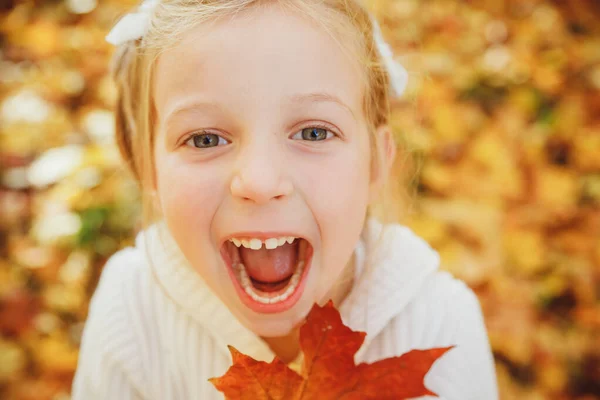 가을 나뭇잎을 가지고 노는 행복 한 어린 소녀. 가을에 입을 벌리고 있는 웃긴 소녀가 감성적 인 얼굴을 하고 있는 사랑 스러운 소녀의 초상을 닫아 버리 세요. 웃는 아이. — 스톡 사진