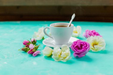 Tomurcuklu düz kompozisyon çiçekleri ve renkli arka planda bir fincan kahve. Kopya Mekan. Sevgililer günü, doğum günü, anne ya da düğün tebrik kartı. Samimi ve romantik kahvaltı.