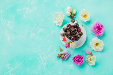 Çiçek açan çiçeklerle ve mavi arka planda böğürtlenli bardaklarla yapılmış yaratıcı bir düzen. Düz yat, Summer Berry. Yaz konsepti. Tatlı, olgun, sulu, tatlı vişne.