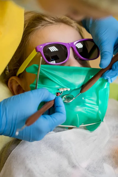 Dentist performing dental filling procedure to preteen girl in pediatric dental clinic. Doctor removing caries using high-speed dental drill. Child in the dental chair dental treatment during surgery.