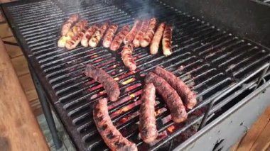 Sosis ızgarada kızarıyor. Adam elinde maşayla ızgarada ızgara sosisleri çeviriyor. Lezzetli sosisler ateşte ızgara yapıyor.
