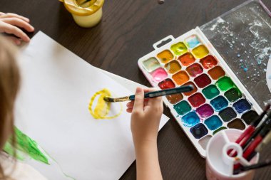 İlk çizim için renk seçiyorum. Suluboya kutusu, çocuklar el ve boya fırçası. Çocuk elleri resim malzemeleriyle resim yapıyor. Resim yapmayı öğreniyor. Scholl dersi
