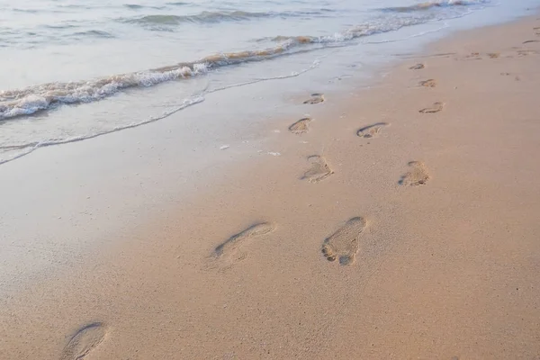 Footprints in the sand at sunset. Beautiful sandy tropical beach with sea waves. Footsteps on the shore.Sea, waves and footprints on the yellow sand on the beach.Soft wave of the sea — Stock Photo, Image