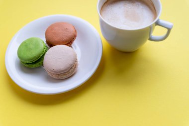 Renkli badem kurabiyesi ve kahve seti. Pastalar, şekerlemeler ve üzerine su sıçratılmış kahve fincanı. Kurabiyeler, kurabiyeler ve kahve fincanı sarısı arka plan. Pastane. Günaydın kart. Boşluğu kopyala