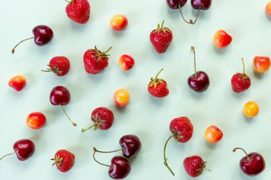 Olgun kiraz ve çilekli renkli parlak desen. Üst görünüm. Dikensiz desen, pastel arka planda çilek ve renkli kirazlar, yaz desenleri. Minimum meyve kavramı.