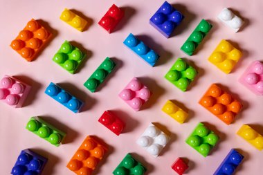 Kalıplar, renkli çocuk inşaatçıları, anaokulları için eğitici bir oyun. Çocuk inşaatçılarının yapı taşlarıyla yapılmış bir oyuncak geçmişi. Pembe arka planda parlak plastik yapı taşları.