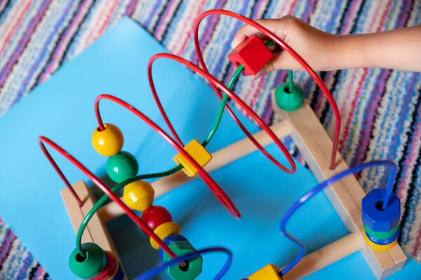 child hand playing and learning with bead roller coaster toy. Selective Focus.Logic toy with paths and spheres, cubes.Kid has fun with Wooden blocks of a bead roller coaster
