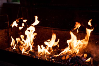 Daha dumanlı kömür dokusu. Ateşin parlak alevleriyle barbekü kömürü ızgarası. Seçici odaklanma. Yanan odun ve kömür